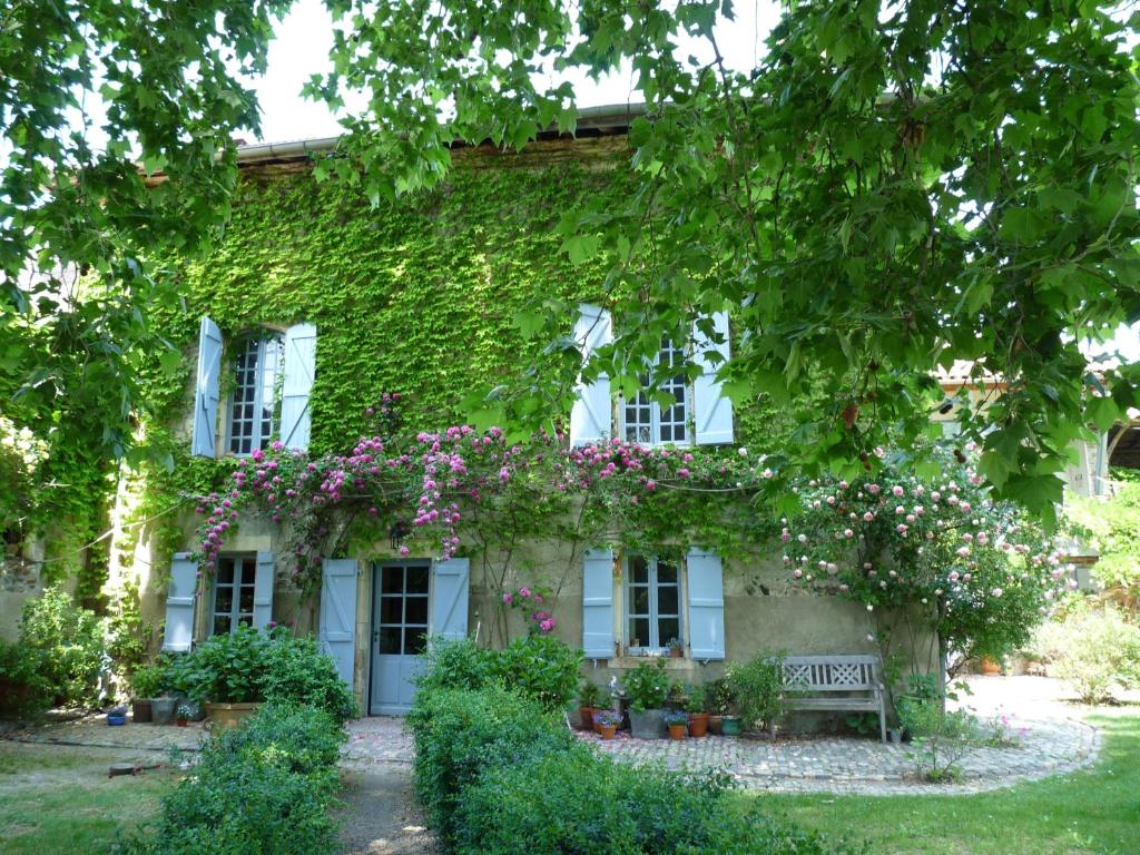 un edificio cubierto de hiedra con un banco y flores en Chambres d'hôtes Les Pesques, en Palaminy