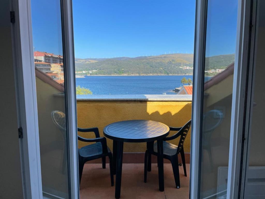a table and chairs on a balcony with a view of the water at Apartamento en la Playa de Quenxe in Corcubión