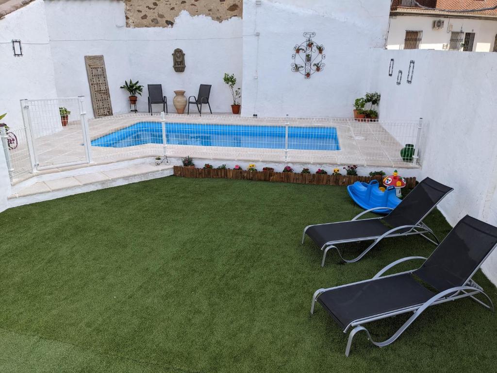 a swimming pool with two chairs and a grass yard at Casa Rural Almenas del Cid in Almonacid de Toledo