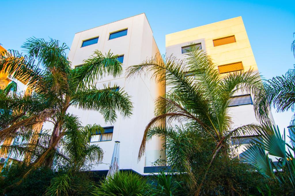 biały budynek z palmami przed nim w obiekcie Apartamentos 16:9 Suites Almería w mieście Almería