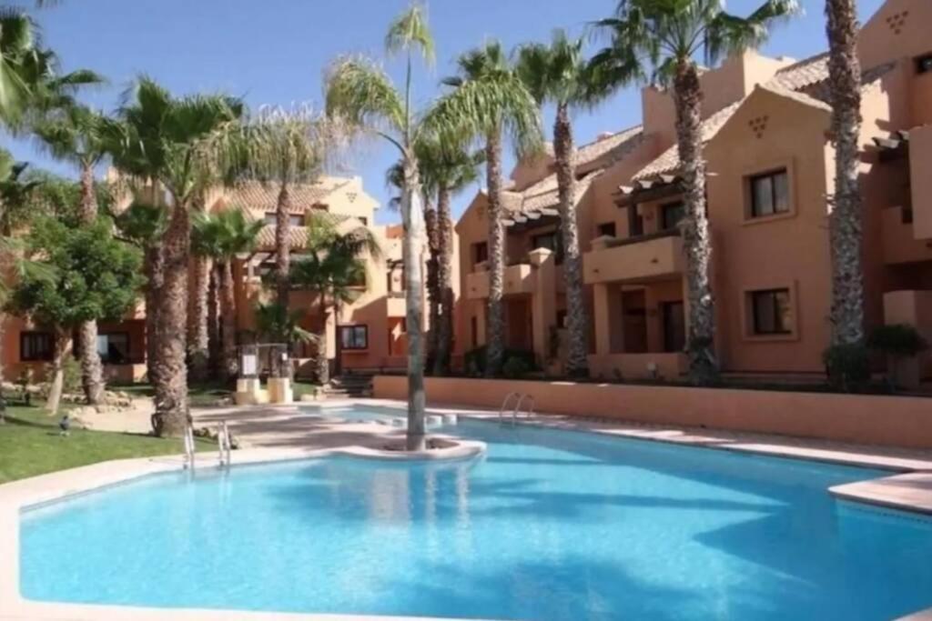 a swimming pool in front of a building with palm trees at Lovely and luxury apartament in front of the beach in Los Alcázares