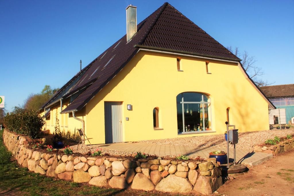 a yellow house with a black roof and a stone wall at Familienfreundliche Ferienwohnung am Reuterteich in Seedorf