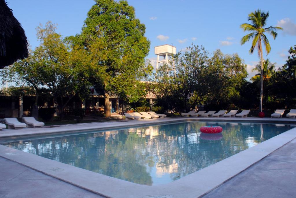a swimming pool with chairs and trees and a building at Hotel Puerta Chichen in Chichén-Itzá