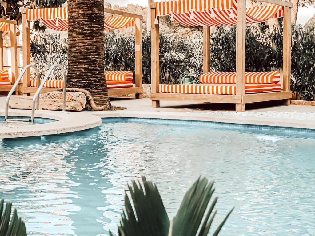 a swimming pool with orange and white chairs and a palm tree at Villa Piccola by Cassai in Colònia de Sant Jordi