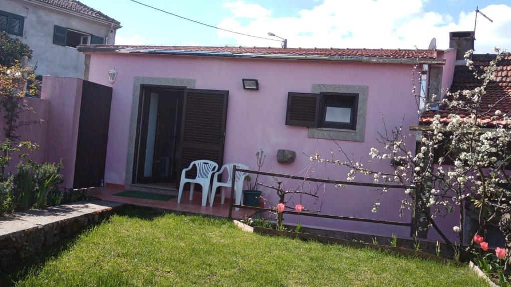 a small pink house with two chairs in the yard at Pêssego - AL in Arouca