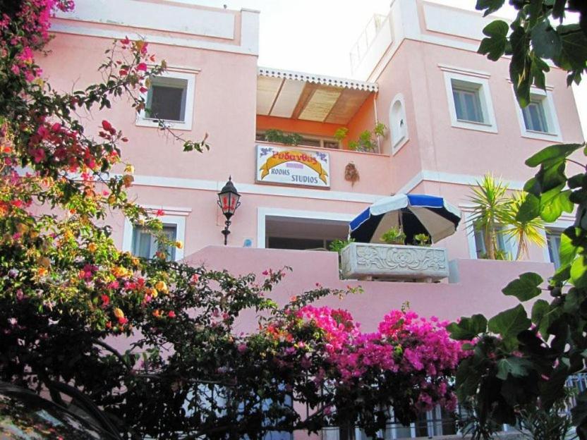 um edifício cor-de-rosa com um guarda-chuva e flores à sua frente em Villa Rodanthos em Perdika