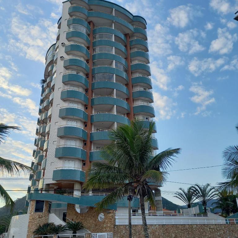 a tall building with a palm tree in front of it at Ótimo apartamento condomínio frente a praia in Mongaguá