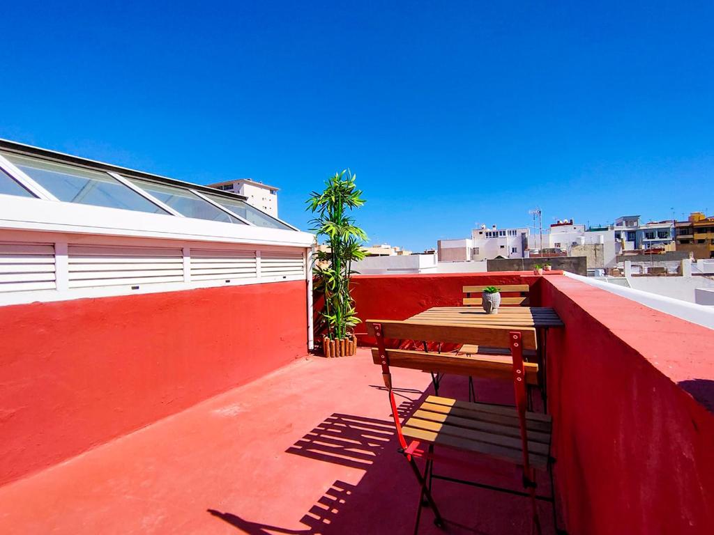 un banco de madera en una pared roja en un balcón en Alma Canaria Apartments & Rooms, en Las Palmas de Gran Canaria