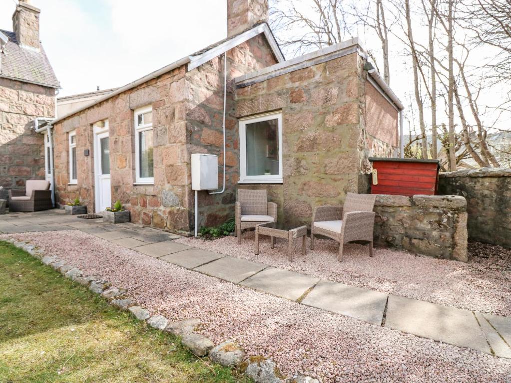 a stone house with two chairs and a window at Gairnlea Cottage in Ballater