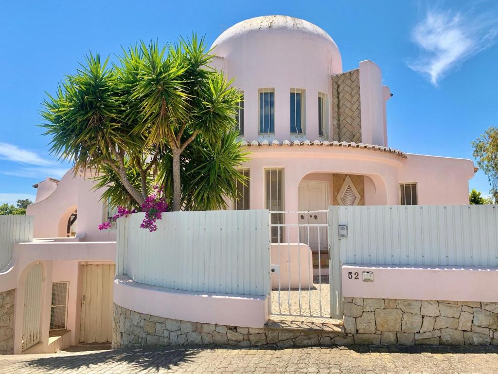 ein rosafarbenes Haus mit einem Zaun und einer Palme in der Unterkunft Villa Amendoeiras 52 in Albufeira