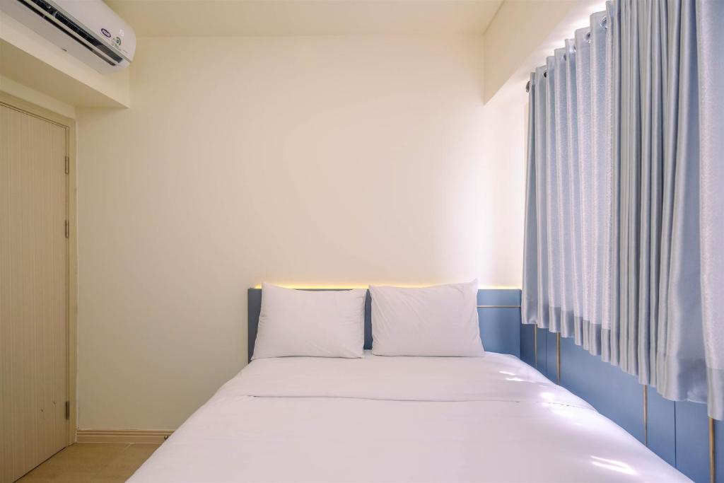a bedroom with a bed with white sheets and a window at Comfort and Strategic 3BR Meikarta Apartment By Travelio in Cikarang