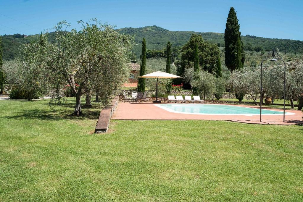 een zwembad met een parasol, stoelen en bomen bij La Casa delle Rose in Terranuova Bracciolini