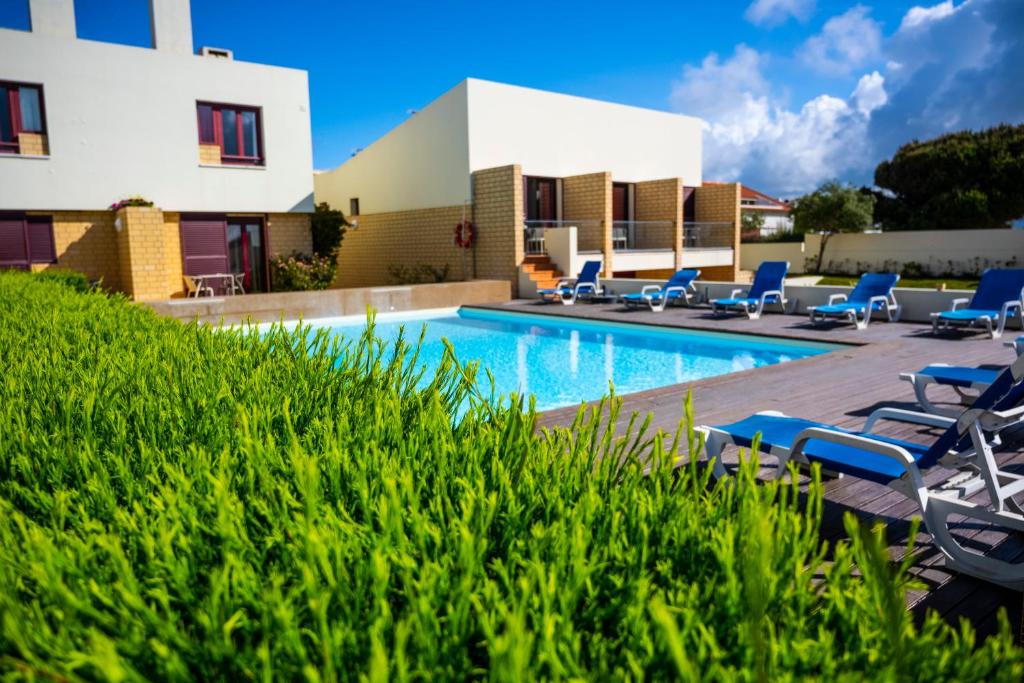 a swimming pool with lounge chairs and a building at Hotel Apartamento Porto Covo in Porto Covo