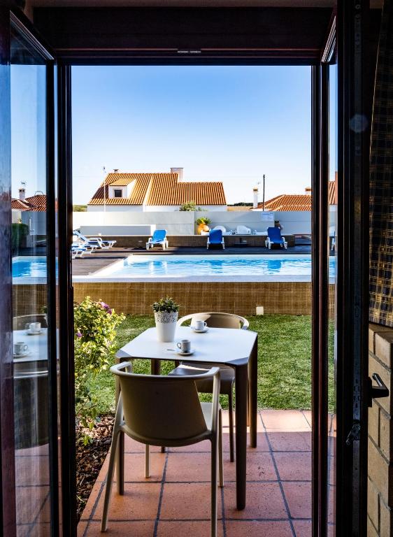 a table and chairs on a patio with a view of a pool at Hotel Apartamento Porto Covo in Porto Covo