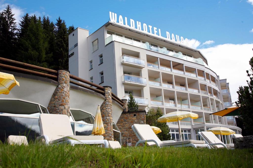 Waldhotel & SPA Davos - for body & soul في دافوس: فندق فيه كراسي ومظلات امام مبنى
