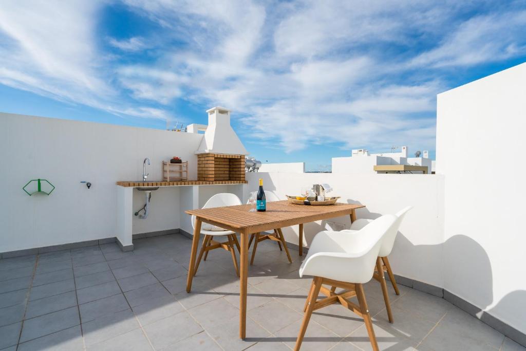 un patio con mesa de madera y sillas blancas en T2 in Alvor with Rooftop Terrace & Pool, en Alvor