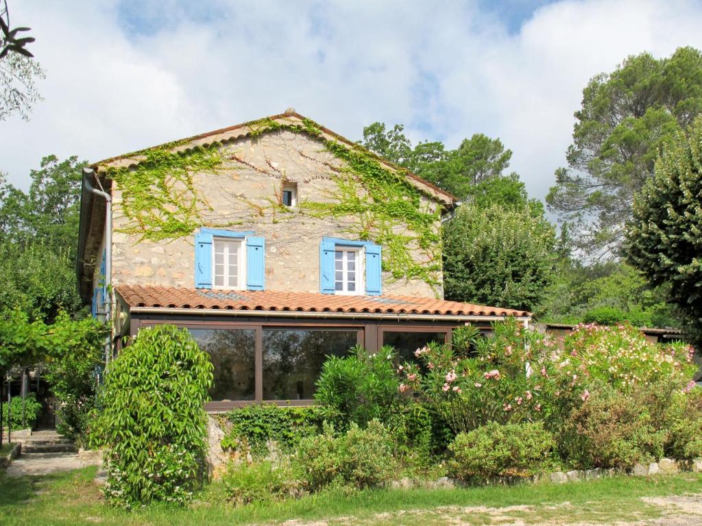 een oud stenen huis met blauwe ramen en struiken bij Holiday Home Mas de l'Adrech by Interhome in Fayence