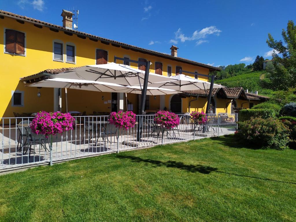 un edificio giallo con tavoli e ombrelloni in un cortile di La Bossolasca Albergo Ristorante a Santo Stefano Belbo