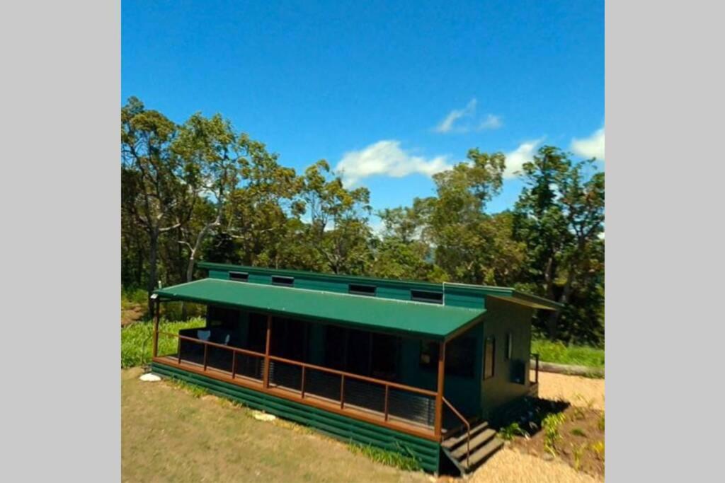 ein kleines Gebäude mit einem grünen Dach auf einem Feld in der Unterkunft Ridge Cabin - Stunning Views - 5km From Neighbours in Airlie Beach