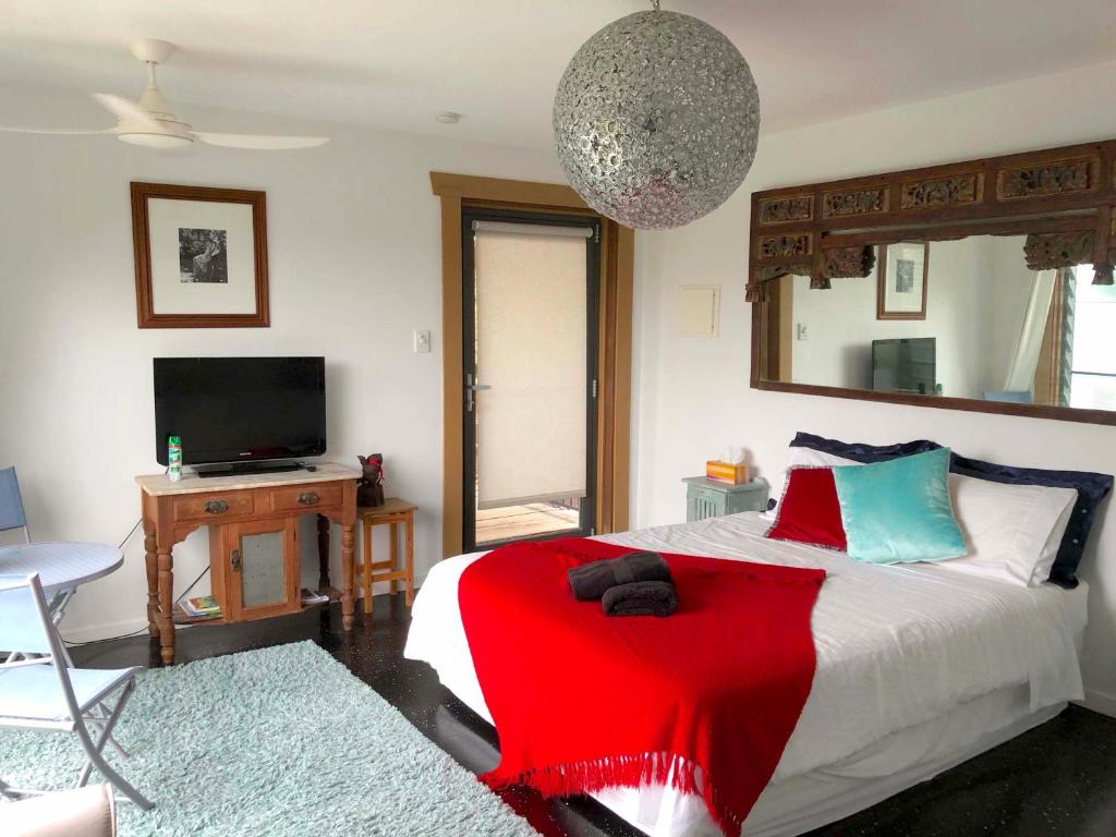 Schlafzimmer mit einem Bett mit einer roten Decke und einem TV in der Unterkunft THE GOLDEN RETREAT POOL HOUSE in Uki