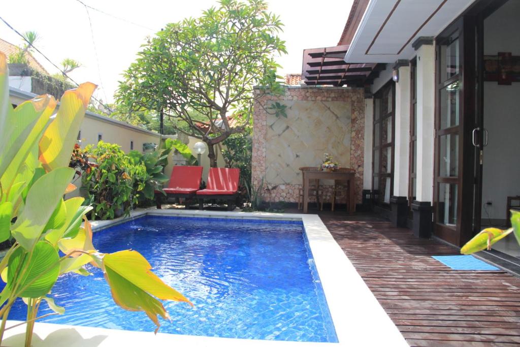 a swimming pool in a yard with red chairs at Ketut Villa Sanur in Sanur