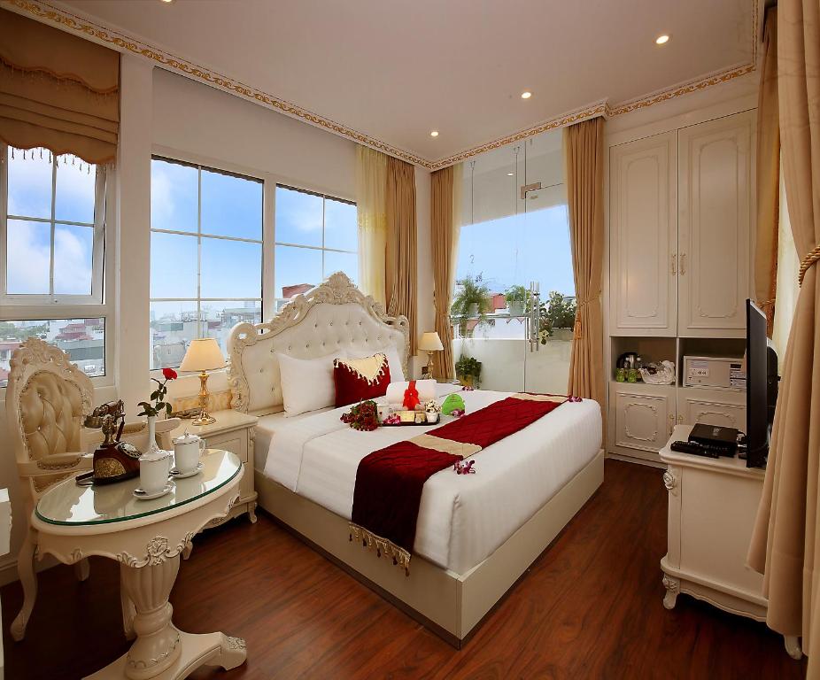 Schlafzimmer mit einem weißen Bett, einem Tisch und Fenstern in der Unterkunft Hanoi Hotel Royal in Hanoi