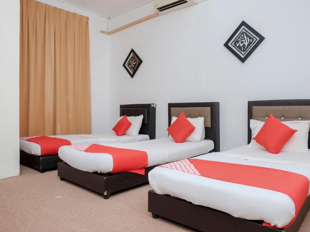 3 camas en una habitación con almohadas rojas y blancas en OYO 90180 Gemilang Hotel Kerteh, en Dungun