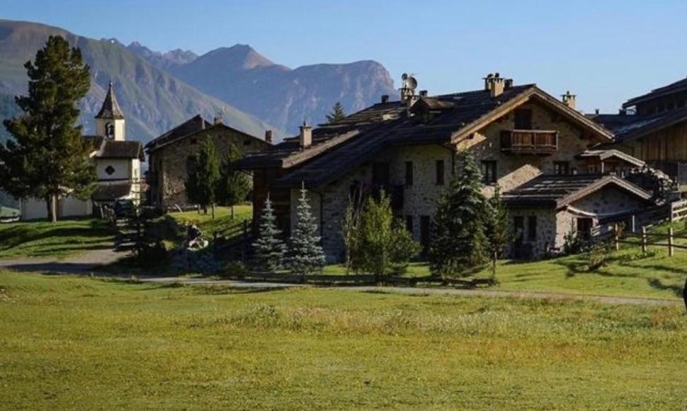 an old house in a field with mountains in the background at Baita Pomo in Livigno
