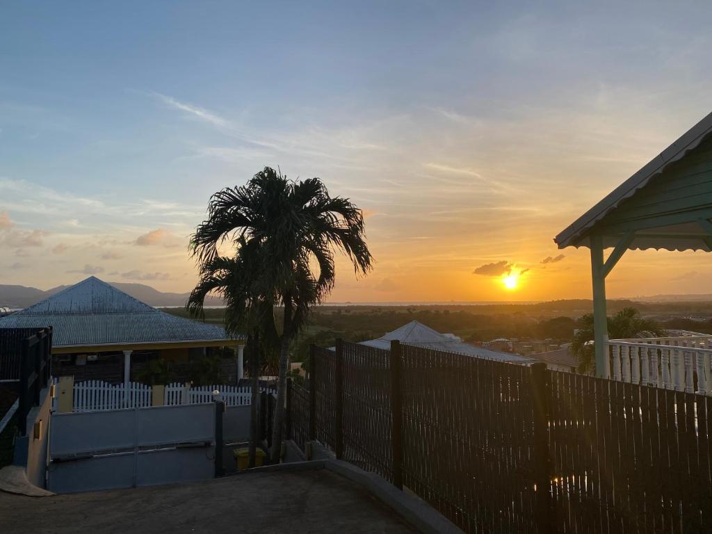 un coucher de soleil depuis une maison avec une clôture et un palmier dans l'établissement La Villa Navidad, à Ducos