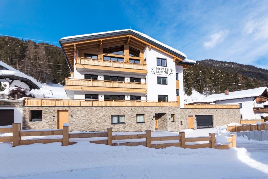 un grand bâtiment dans la neige avec une clôture dans l'établissement Moose Lodge, à Sankt Anton am Arlberg