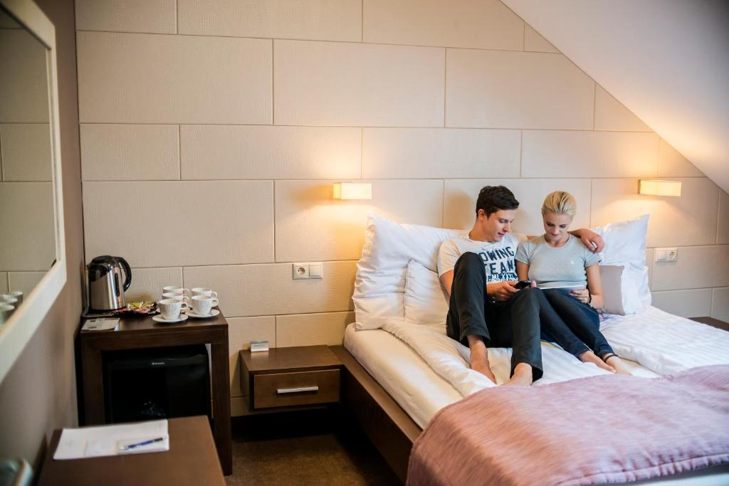 two people sitting on a bed in a hotel room at Hotel Fürdőház in Nyíregyháza