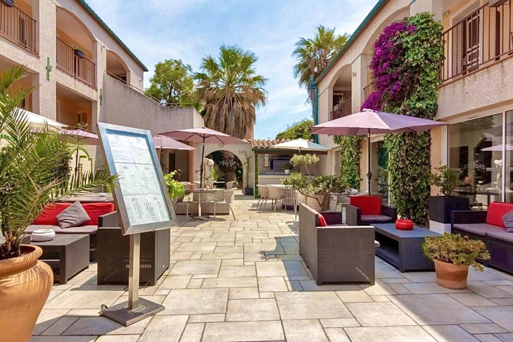 un patio avec des tables, des chaises et des parasols dans l'établissement Logis Hôtel Les II Mas - Perpignan Sud, à Cabestany