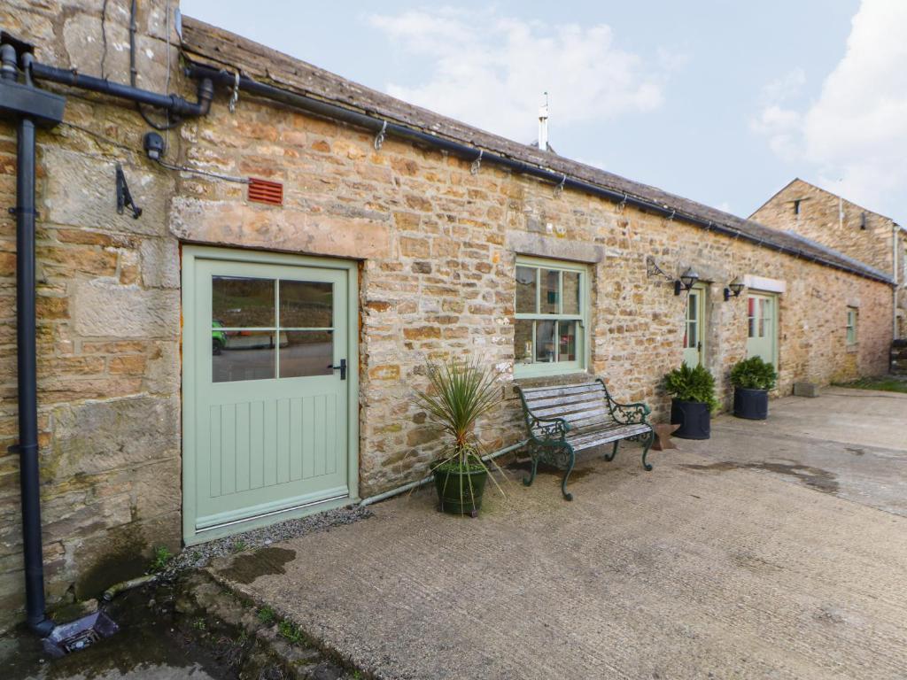 a brick building with a green door and a bench at Low Shipley Cottage in Cotherstone