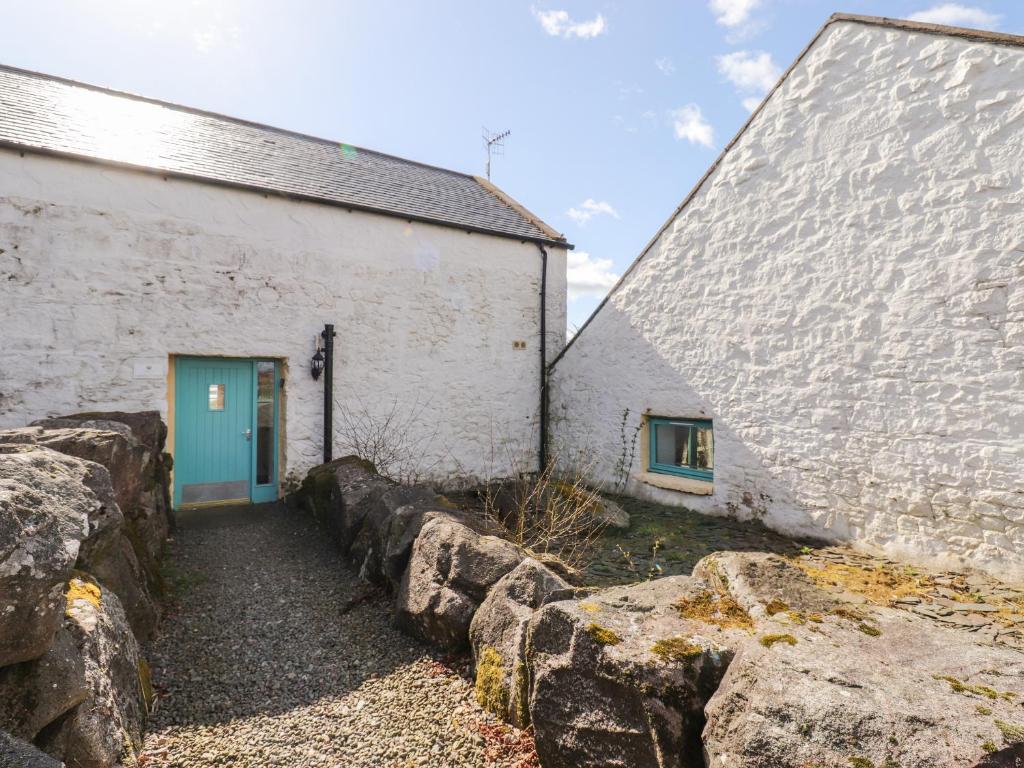 a white building with a blue door and a stone wall at Lapwing Cottage in Dalbeattie