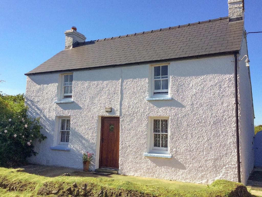 a white house with a brown door on a field at Ty Gwyn in Goodwick