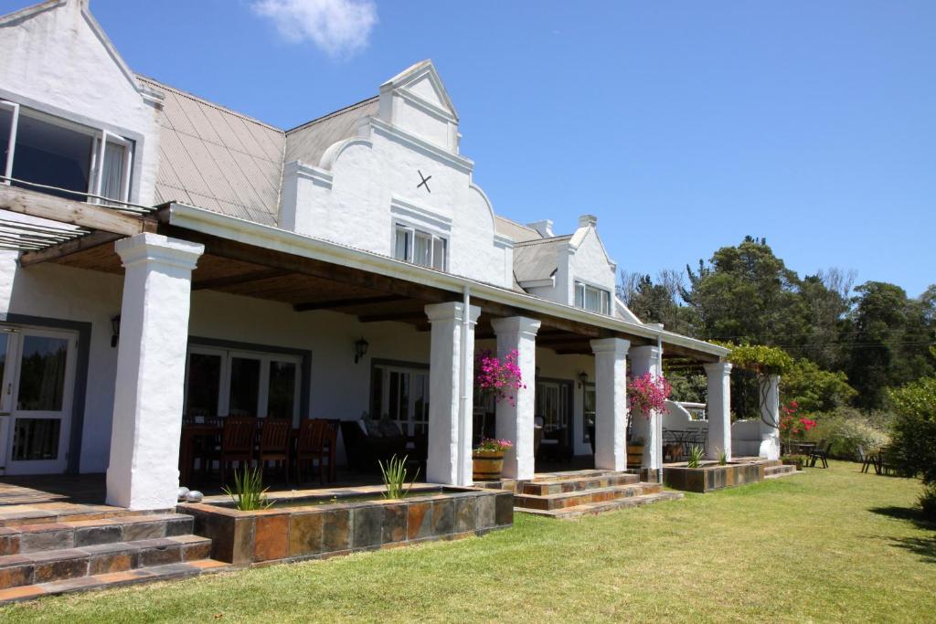 a white house with columns and pink flowers at Fynbos Ridge Country House & Cottages in Plettenberg Bay