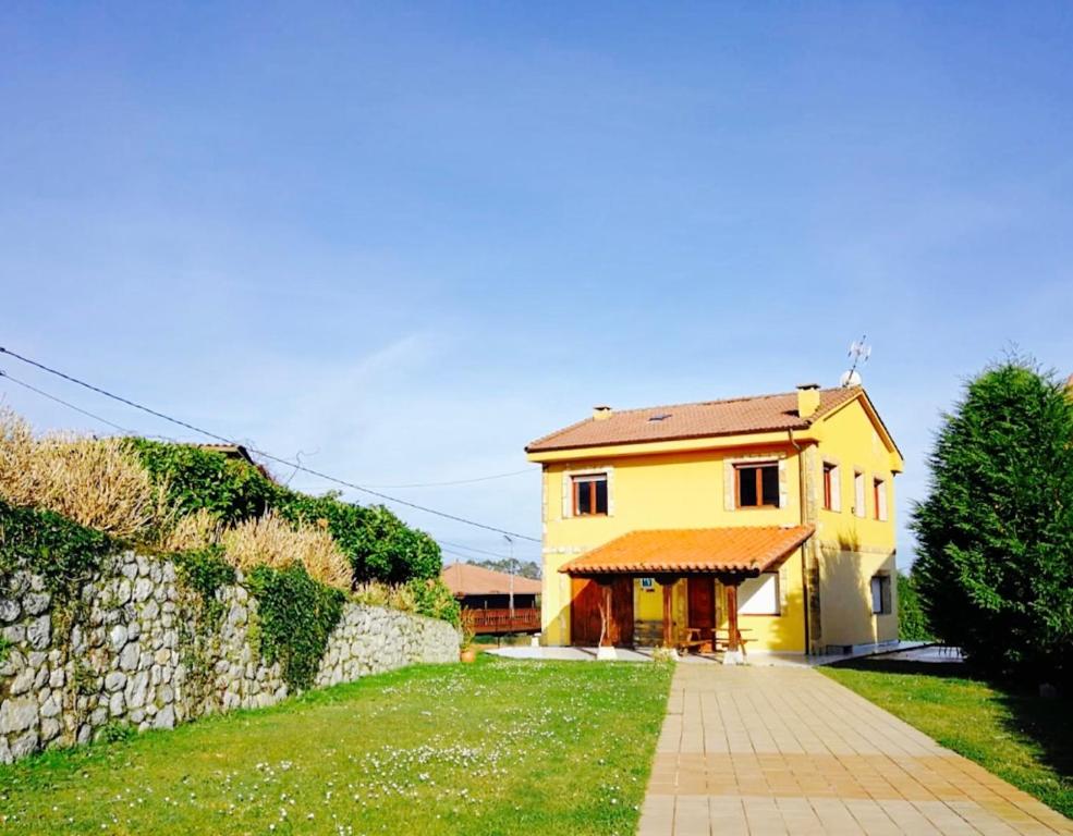 a yellow house with a stone wall and a sidewalk at Casa Las Vistas Llanes in Nueva de Llanes
