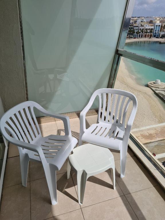 two white chairs and a stool on a balcony at Water's Edge Hotel in Birżebbuġa