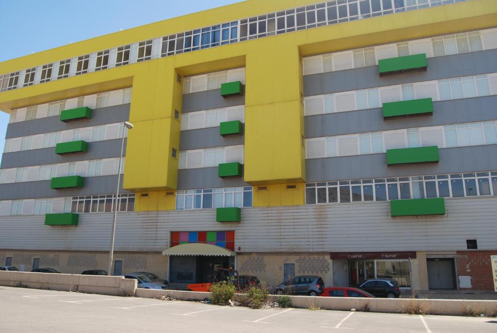 a yellow and gray building with cars parked in a parking lot at Apartamentos Turisticos Mediterraneo in Cartagena