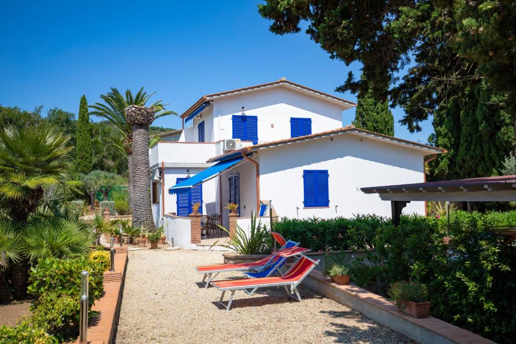 a white house with blue shutters and two lounge chairs at Villa le Palme in Capoliveri