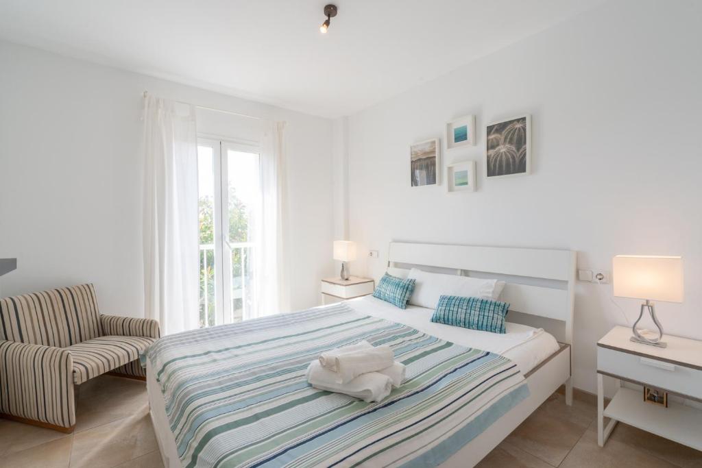 a white bedroom with a bed and a chair at Casa Colonia in Colònia de Sant Jordi