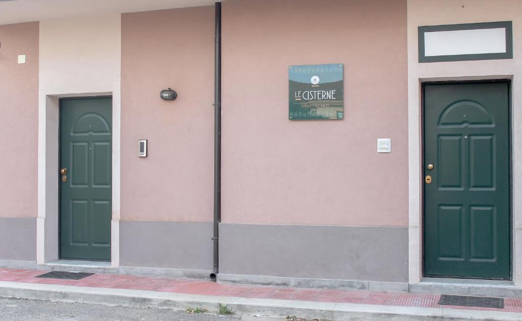 three green doors on a pink building with a sign at Casa Vacanze Le CIsterne in Gioia Tauro