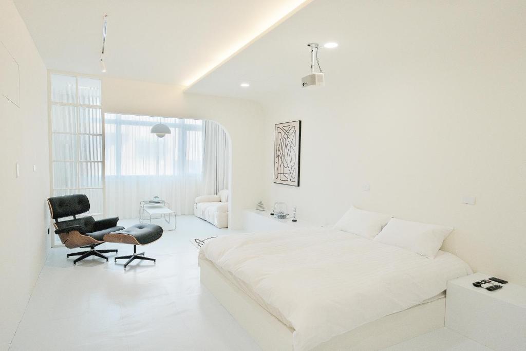 a white bedroom with a bed and a chair at Bianca in Tainan