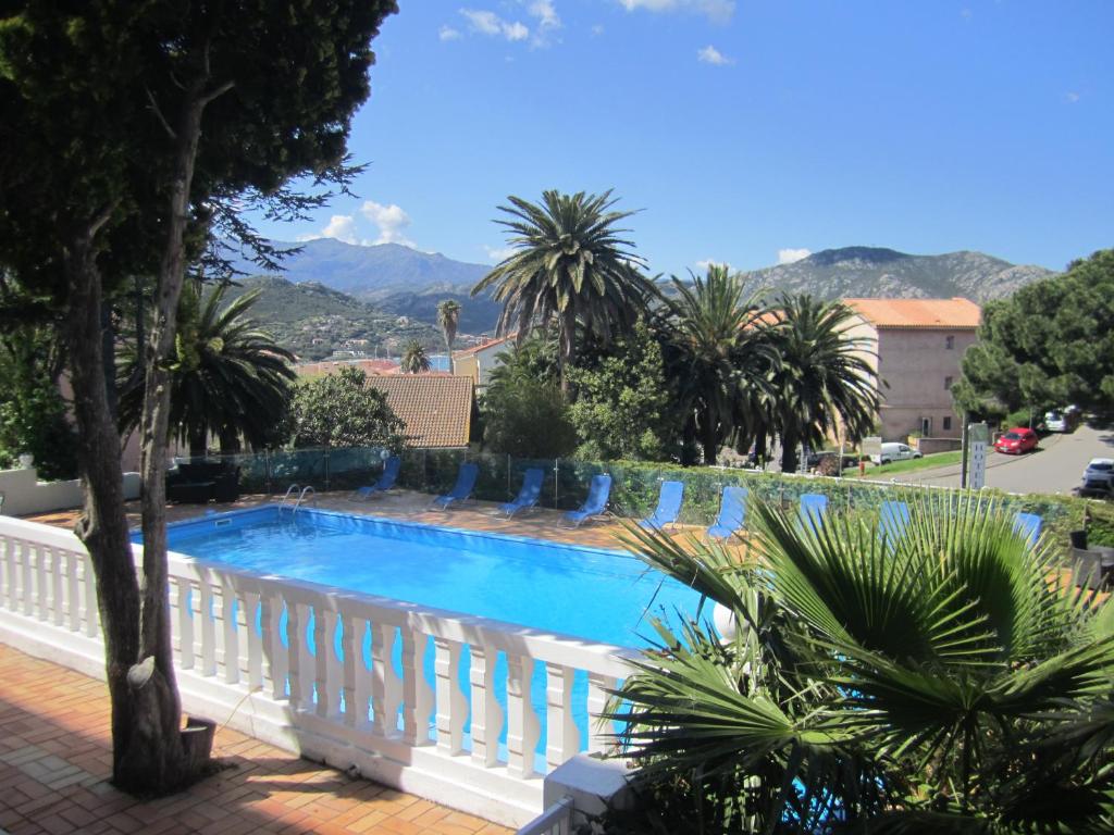 a swimming pool with palm trees and a white fence at Hotel Madame Mere in Saint-Florent