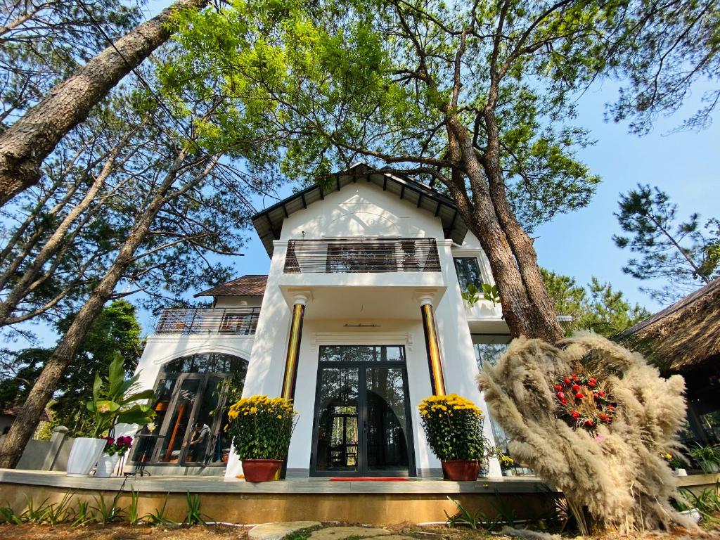 una casa bianca con degli alberi di fronte di S'Nghe Homestay Măng Đen a Kon Von Kla