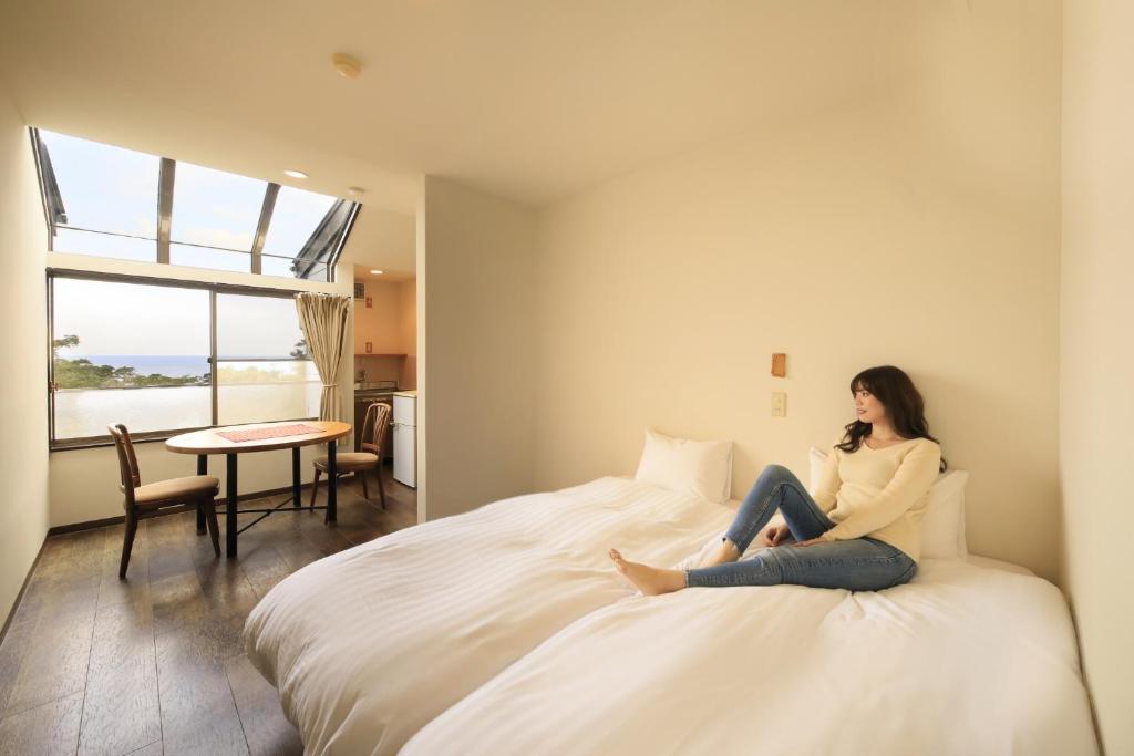 下田市にあるWelcome Inn SunnyStepsの携帯電話で話しながらベッドに座っている女性