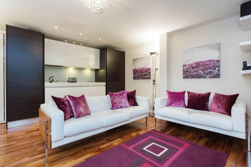 2 divani bianchi in soggiorno con cuscini viola di Veeve - Brilliant Barbican a Londra