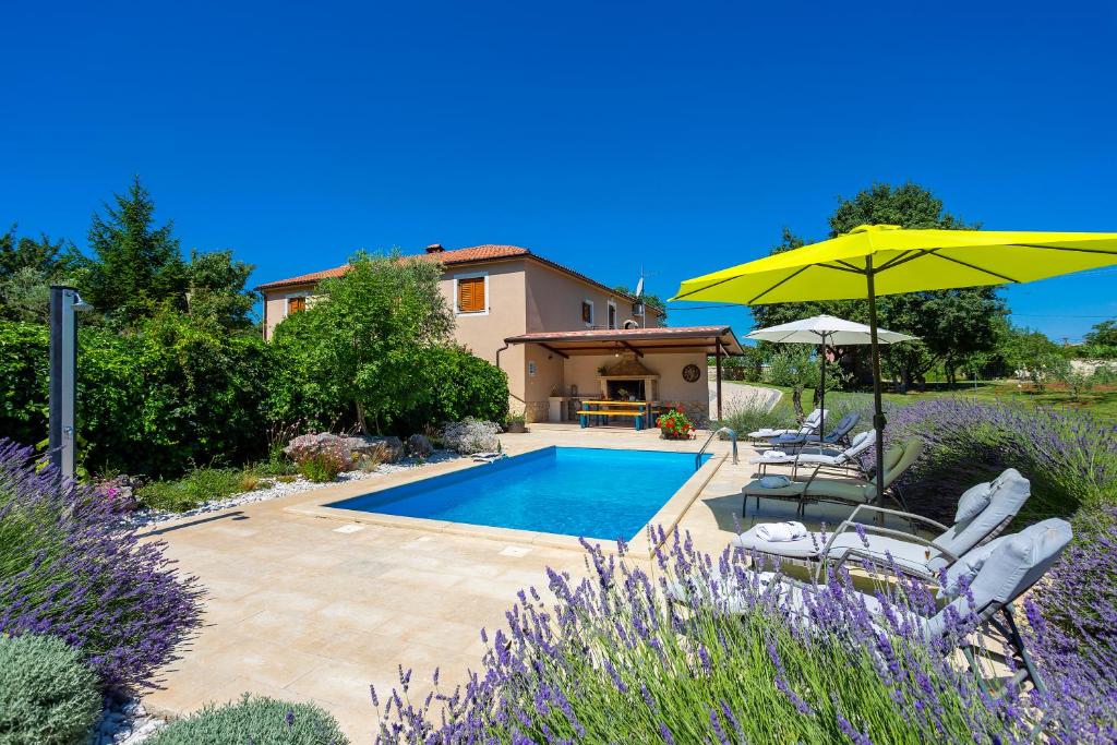 a pool with chairs and an umbrella and a house at Villa Križanci in Žminj