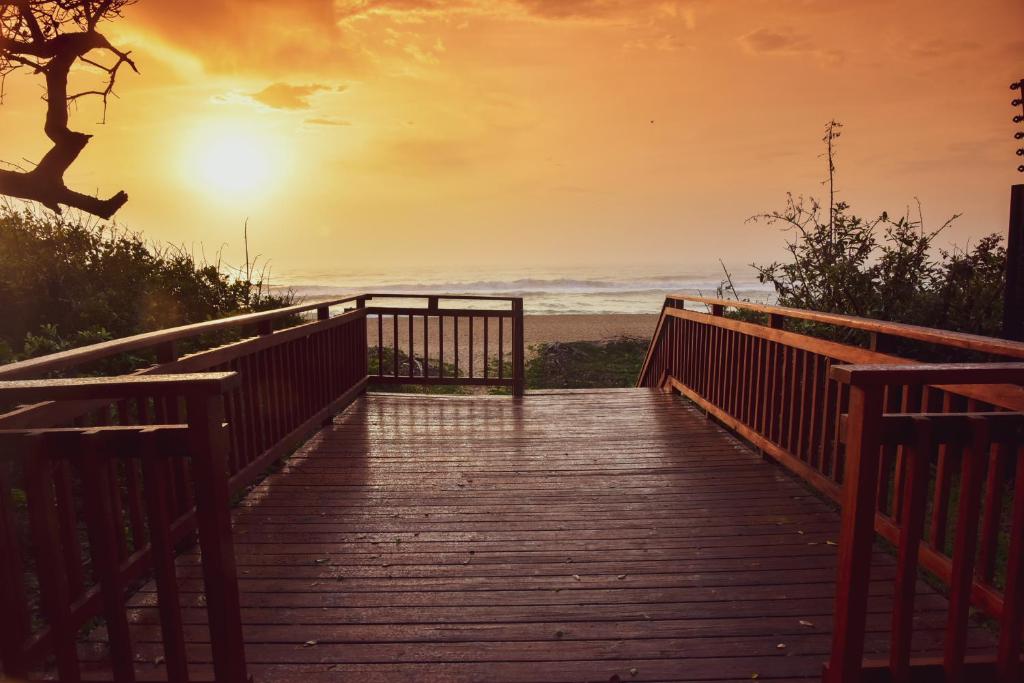 une promenade en bois menant à la plage au coucher du soleil dans l'établissement La Lucia Sands Beach Resort, à Durban