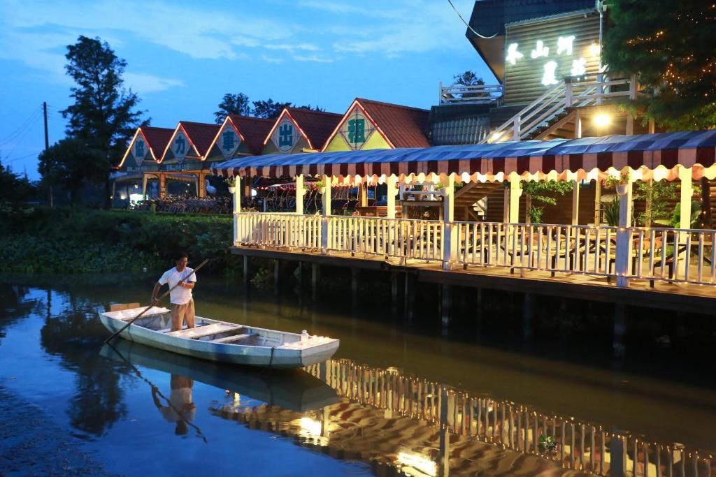 a man in a boat on the water near a restaurant at Dongshan River Resort Farm in Wujie